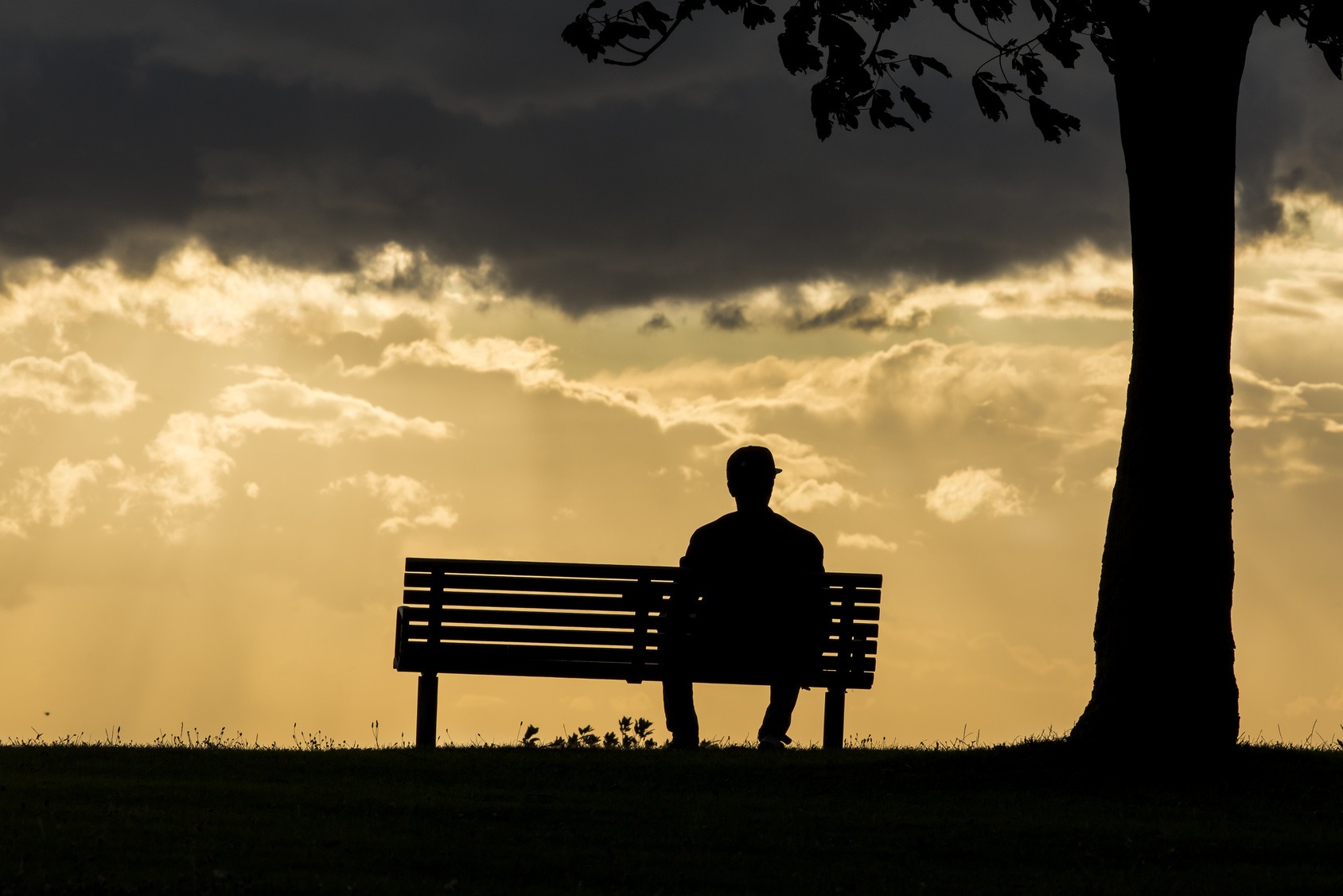 Silhouette of an anonymous male alone on a bench at sunset.